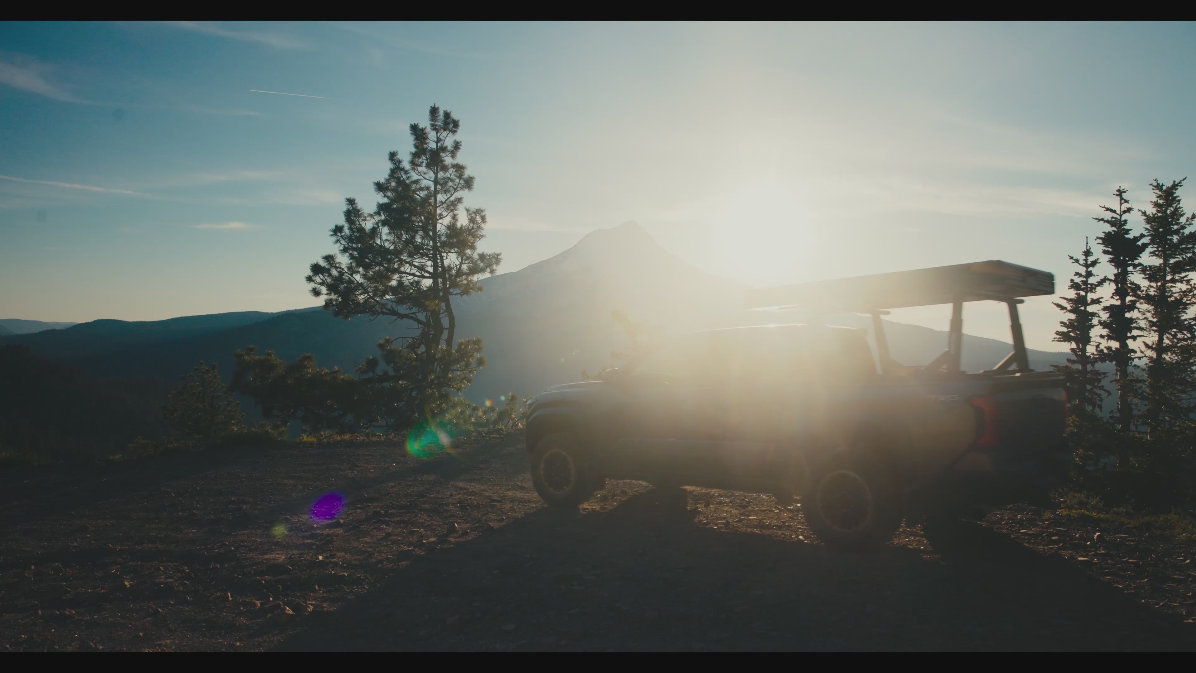 Load video: Truck tolling up in the mountains with a rooftop tent, with the sun setting. Two people are setting up camp for the evening, in an Intrepid Camp Gear tent, as the sun sets b